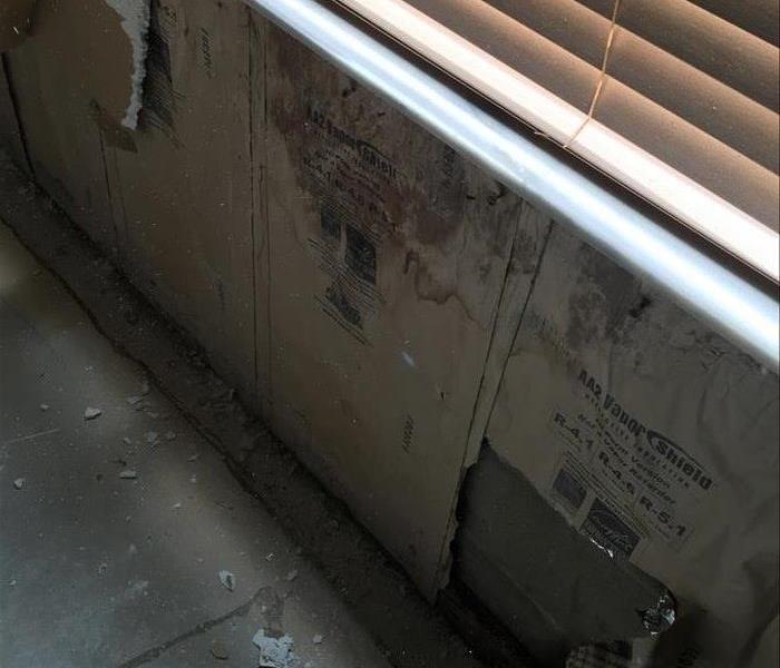 damaged and torn out drywall showing the vapor barrier under a window