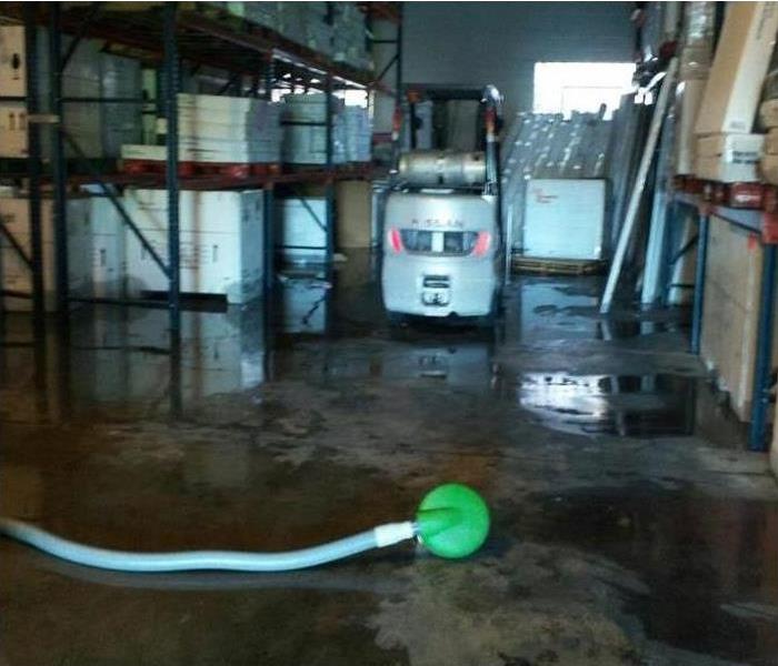 portable pump with hose on warehouse floor, fork truck in background