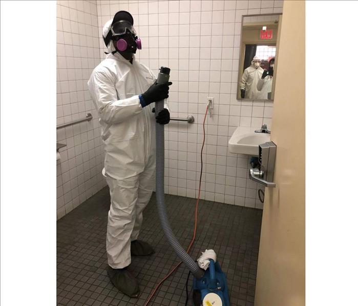 Employee with a mister, clothed in white biohazard suit